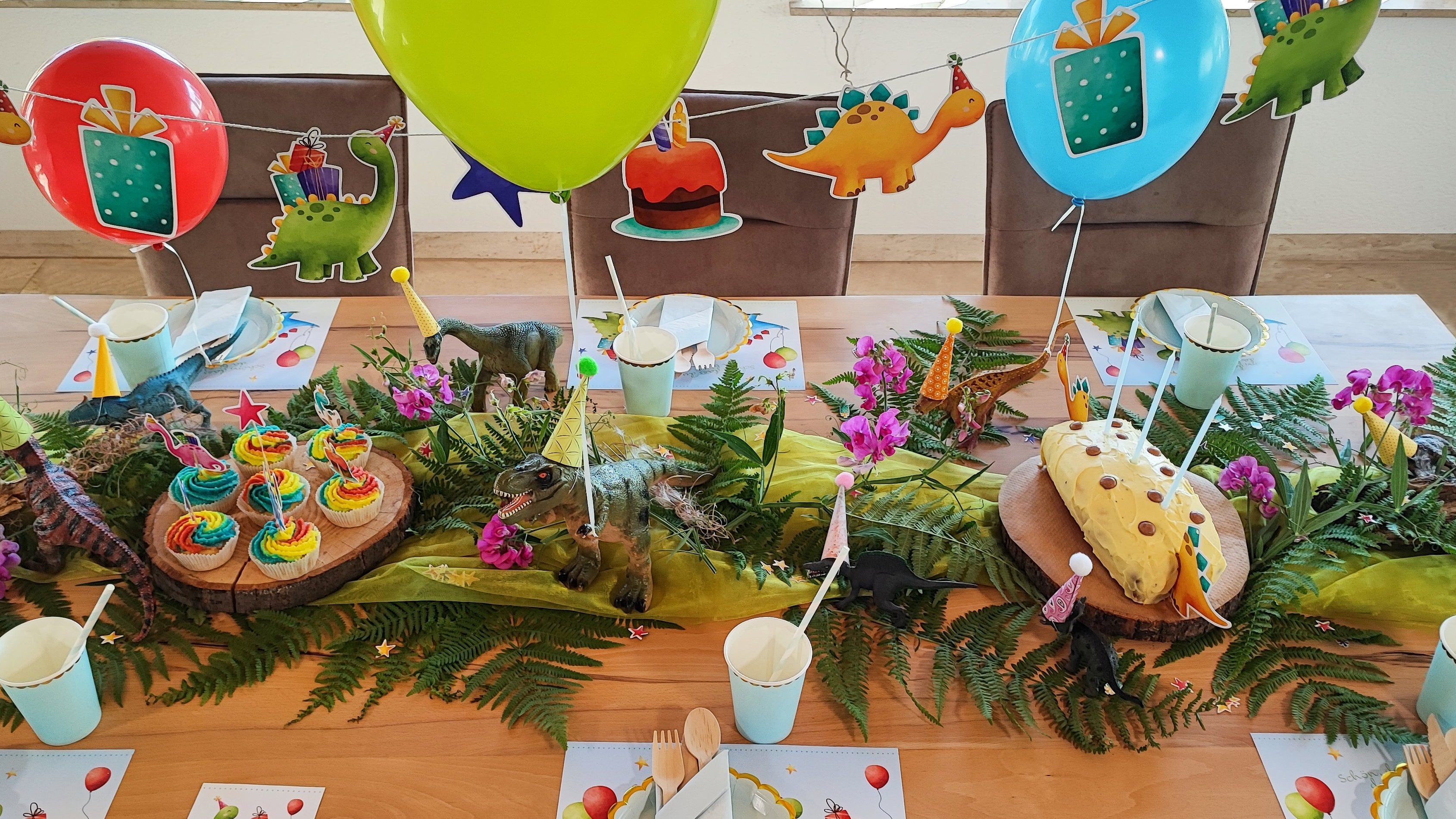 Dekorierter Tisch zum Geburtstag mit Girlanden, Luftballons und Kuchen zum Motto Dinos